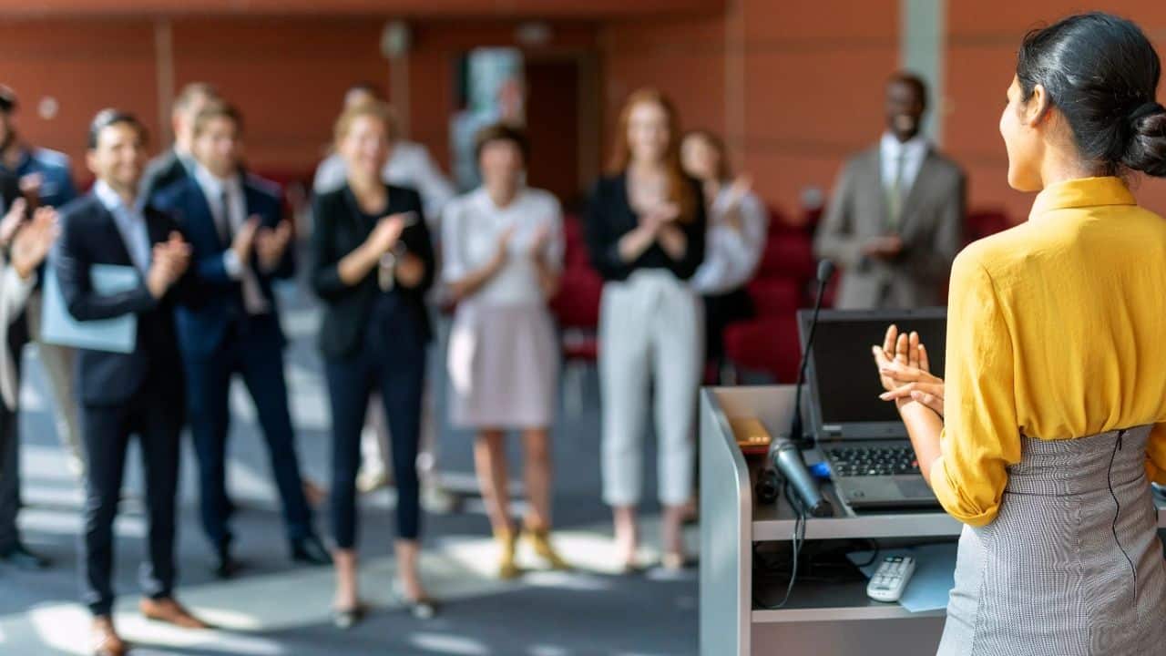 How to present globally, clearly, and with impact, photo of a woman presenting to an audience